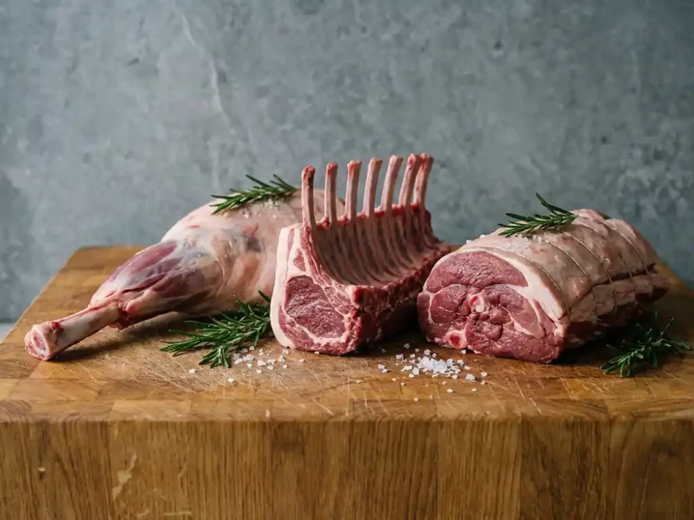Bone-in lamb leg, frenched rack, and rolled shoulder on a rustic butcher block with rosemary and sea salt.