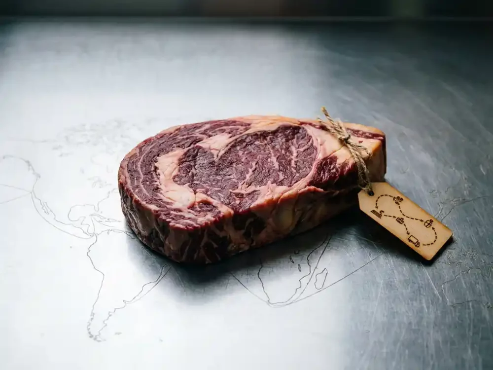 Rohes Rindfleisch auf Edelstahloberfläche mit Herkunftsetikett, das die Lieferkette zeigt, globale Versandrouten im Hintergrund.